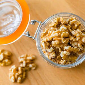 peeled organic walnuts in a glass container shot from above on wood table